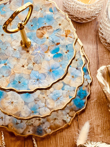 Epoxidharz Etagere mit goldenen Details und blauen sowie beigen Hortensien. Perfekte Kombination aus Eleganz und Funktionalität.