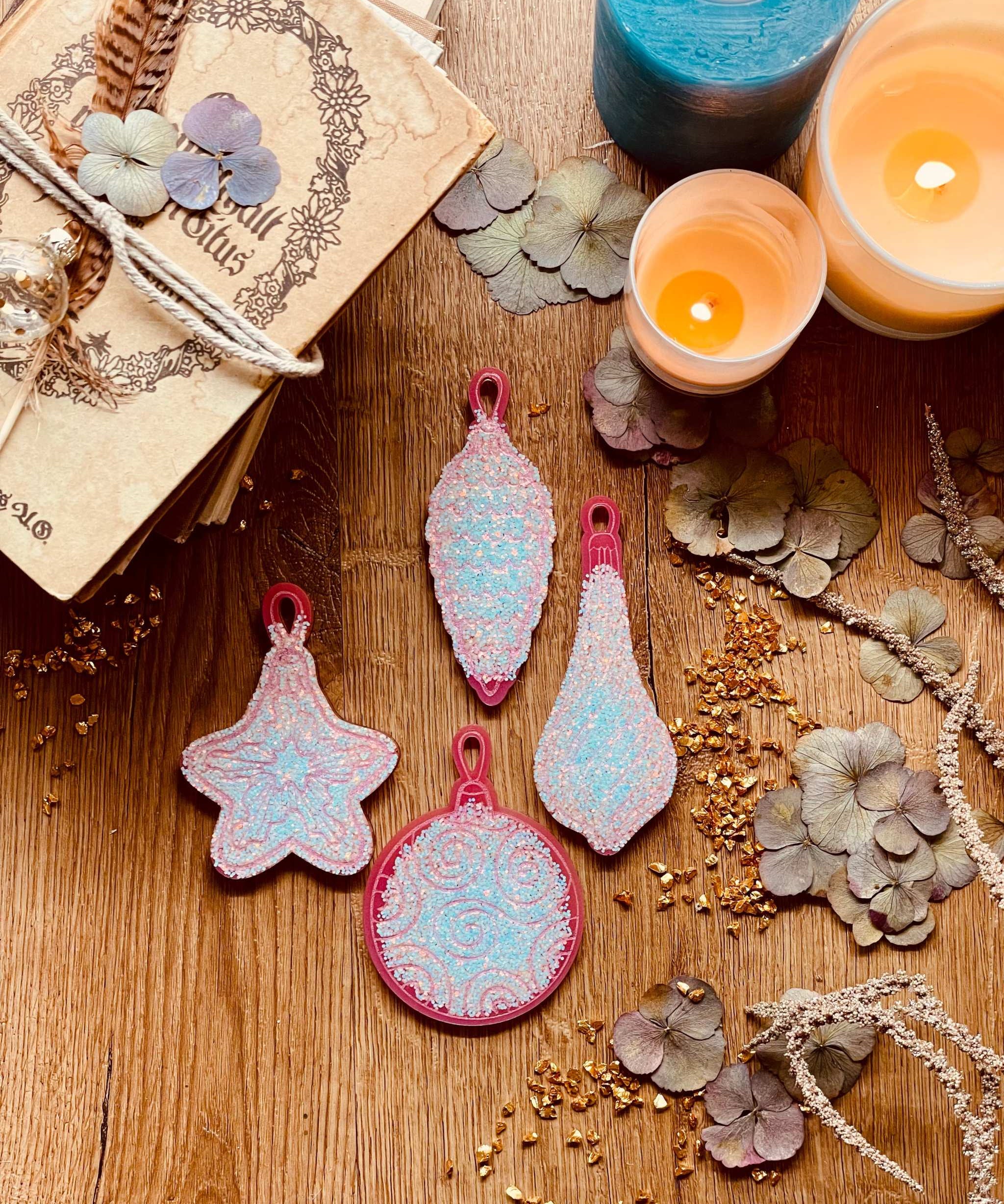 Pink and silver resin Christmas tree ornaments set on a wooden surface, featuring four unique handmade pieces.