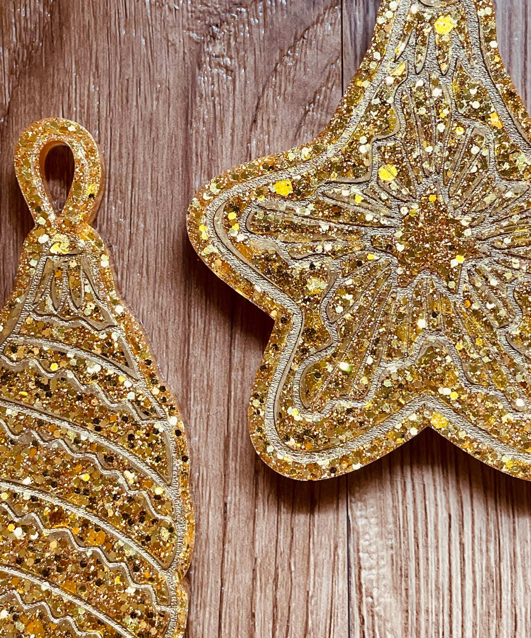 Goldene handgemachte Weihnachtsbaumanhänger aus Resin in Stern- und Tropfenform mit Glitzerdetails auf Holzuntergrund