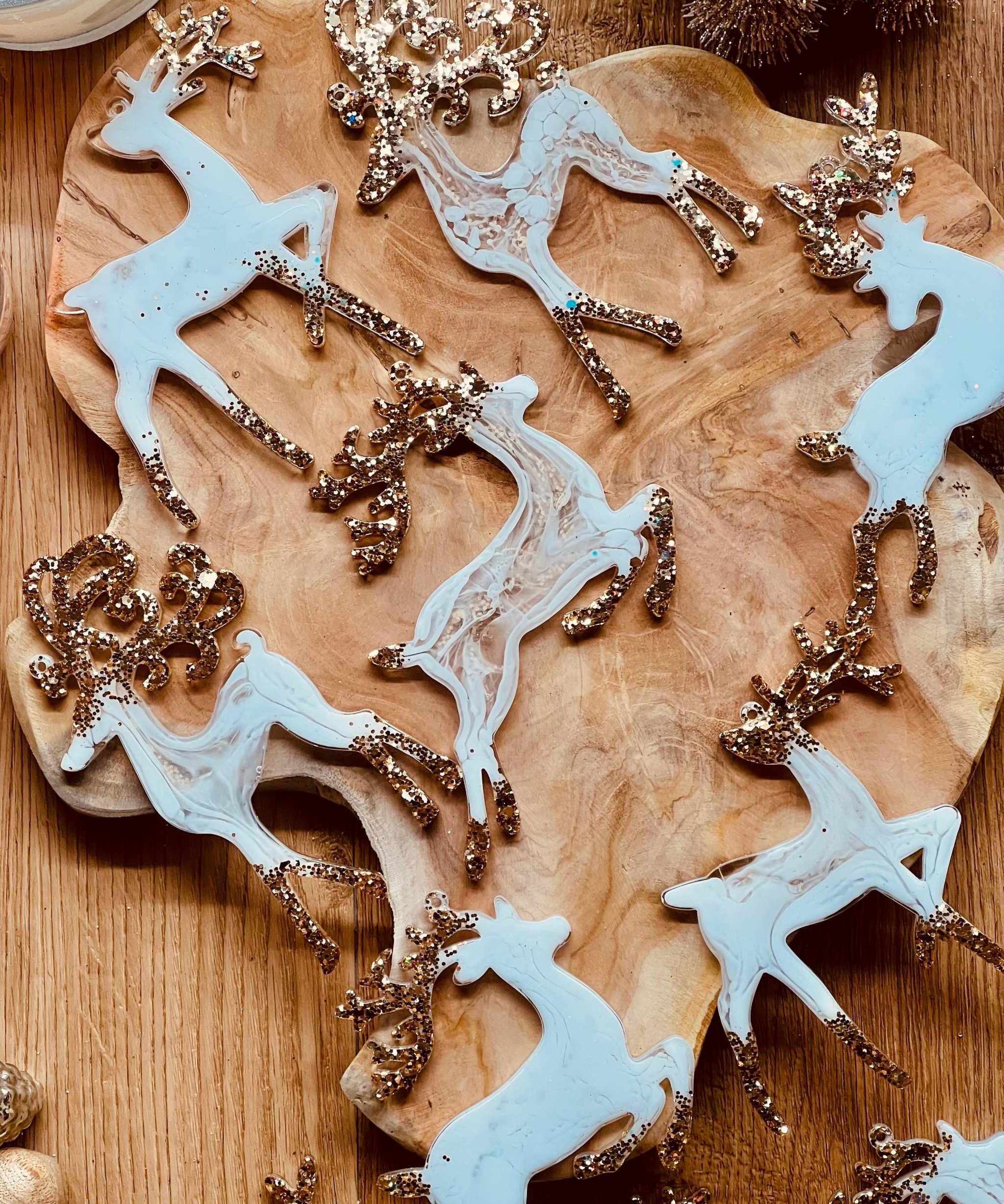 Handmade white and gold resin reindeer Christmas tree ornaments on a wooden background.