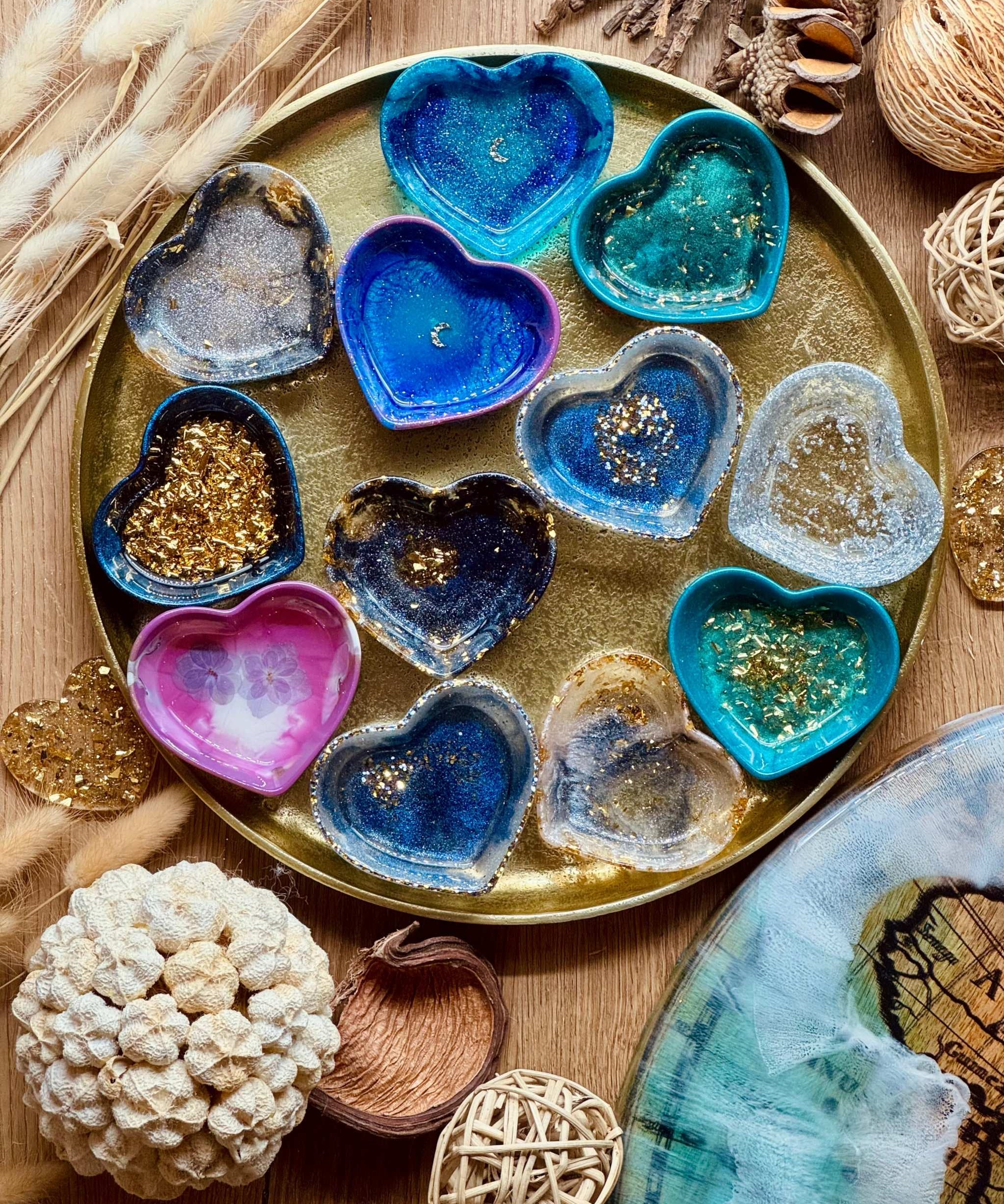 bunte handgemachte Schmuckschalen aus Resin in Herzform mit goldenen Details auf goldfarbenem Tablett