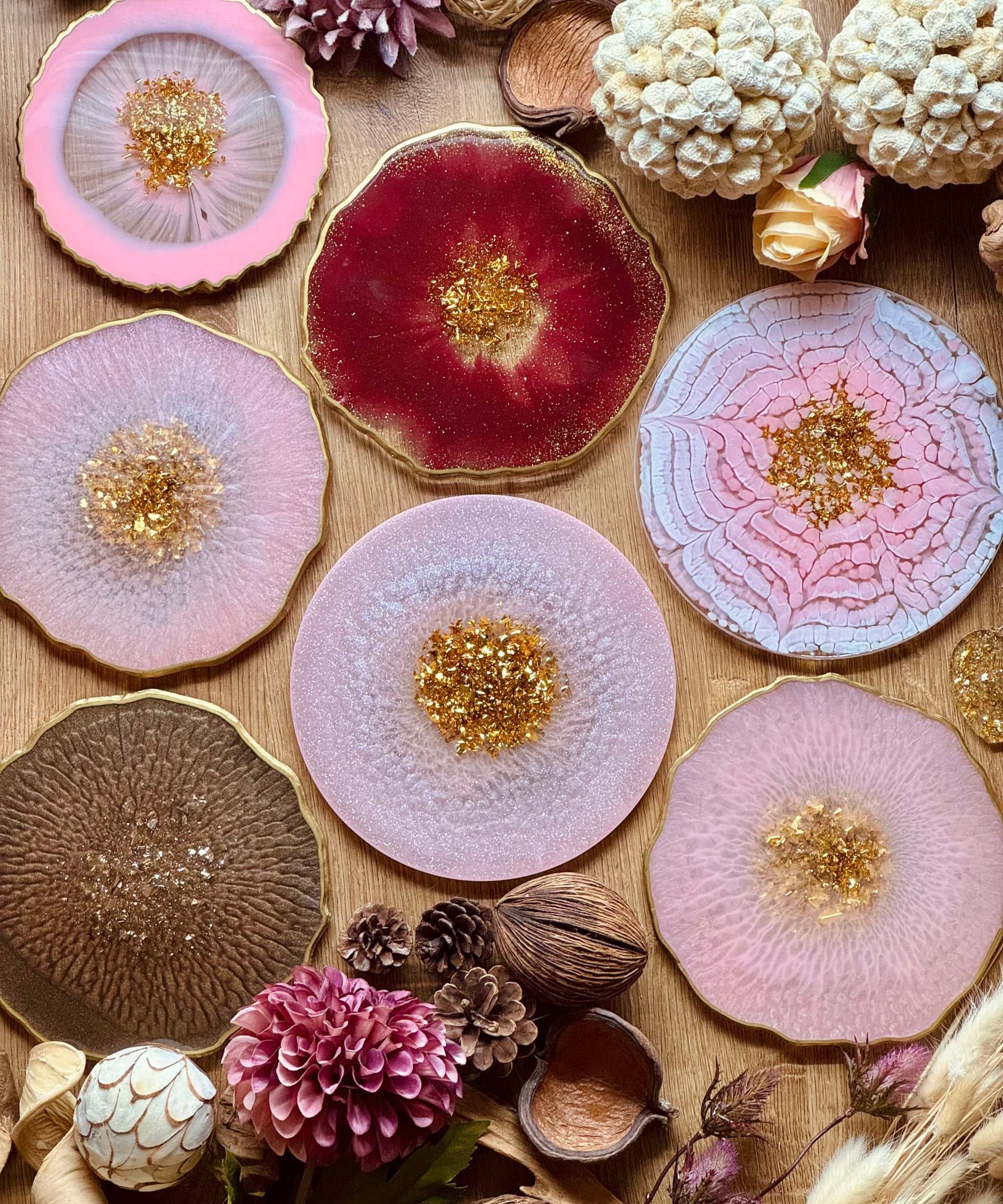 Handgemachte Tabletts aus Resin in rosa, rot und braun mit goldenen Details als dekorative Unikate auf Holztisch mit Naturdeko