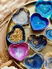 Bunte handgemachte Schmuckschalen aus Resin in Herzform mit goldenen Details auf goldfarbenem Tablett.