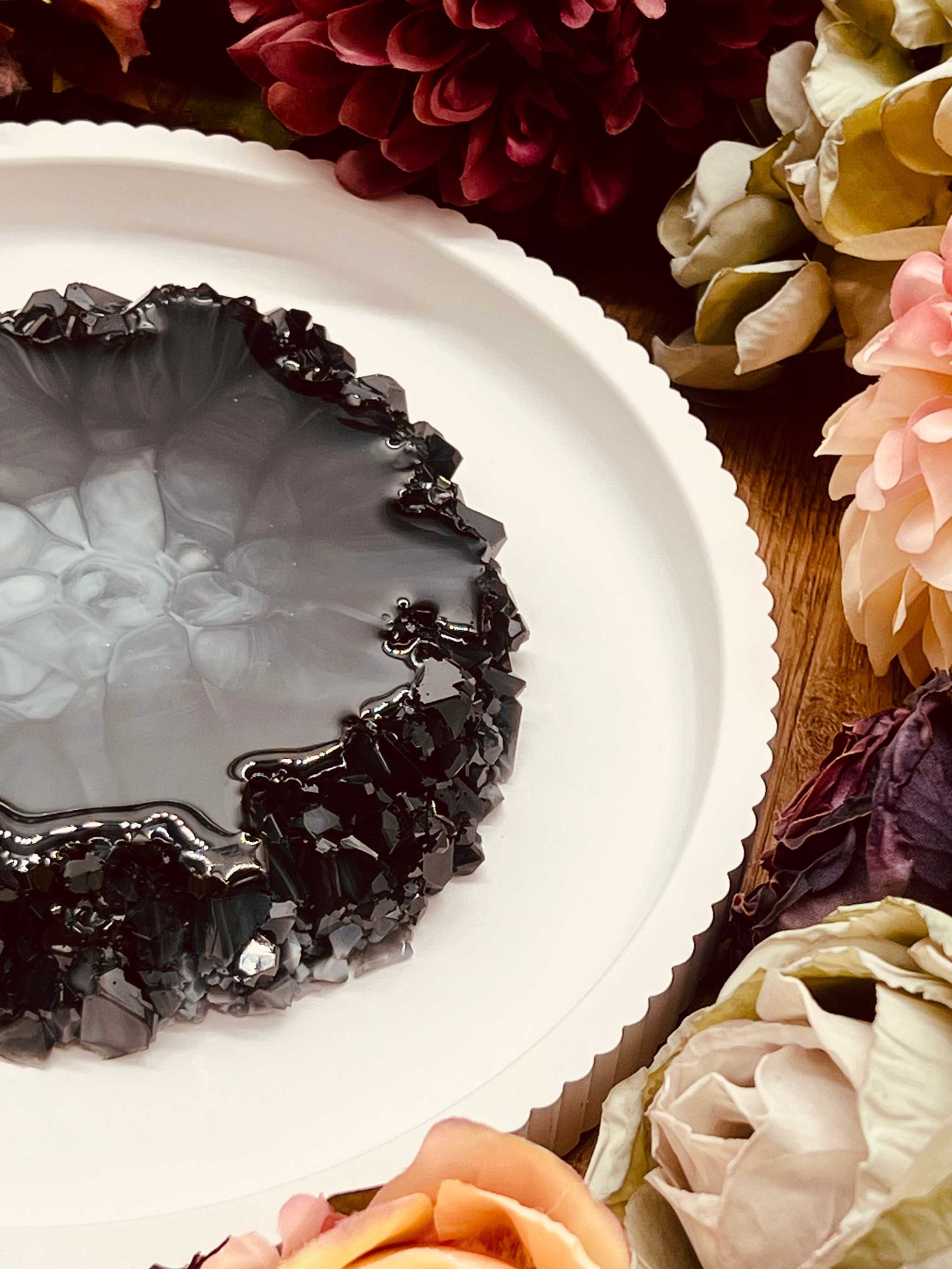 Handgemachtes Tablett aus Resin im Geode Kristall Look, dekorativ und einzigartig, platziert auf weißem Teller mit Blumenarrangement