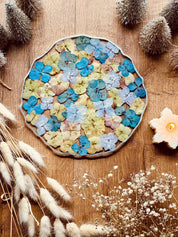 rundes handgemachtes Tablett aus Resin mit bunten Hortensien und silbernen Details auf Holztisch