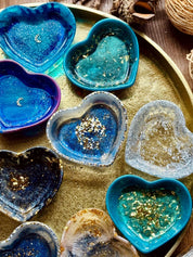 Handgemachte bunte Schmuckschalen aus Resin in Herzform mit goldenen Details auf goldfarbenem Tablett