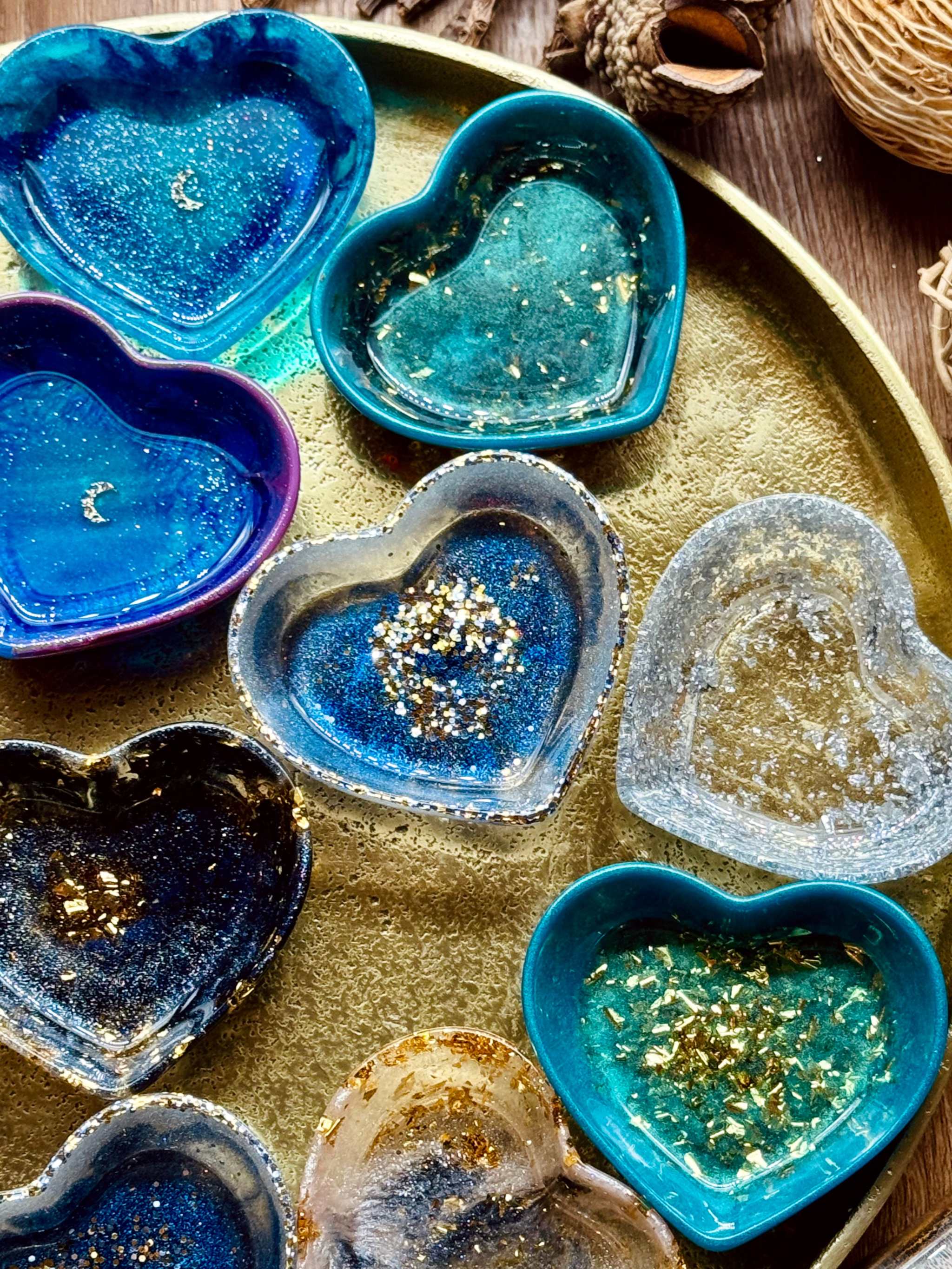 Handgemachte bunte Schmuckschalen aus Resin in Herzform mit goldenen Details auf goldfarbenem Tablett