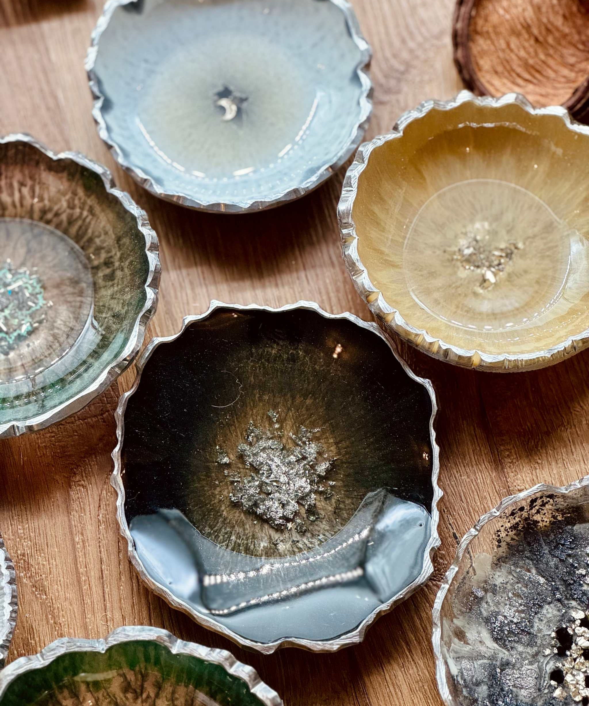 Handgemachte Schmuckschalen aus Resin in verschiedenen Farben mit silbernen Details auf Holztisch
