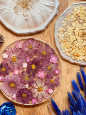 Rundes handgemachtes Tablett aus Resin mit eingebetteten pinken und gelben Blumen und silbernen Details auf Holztisch