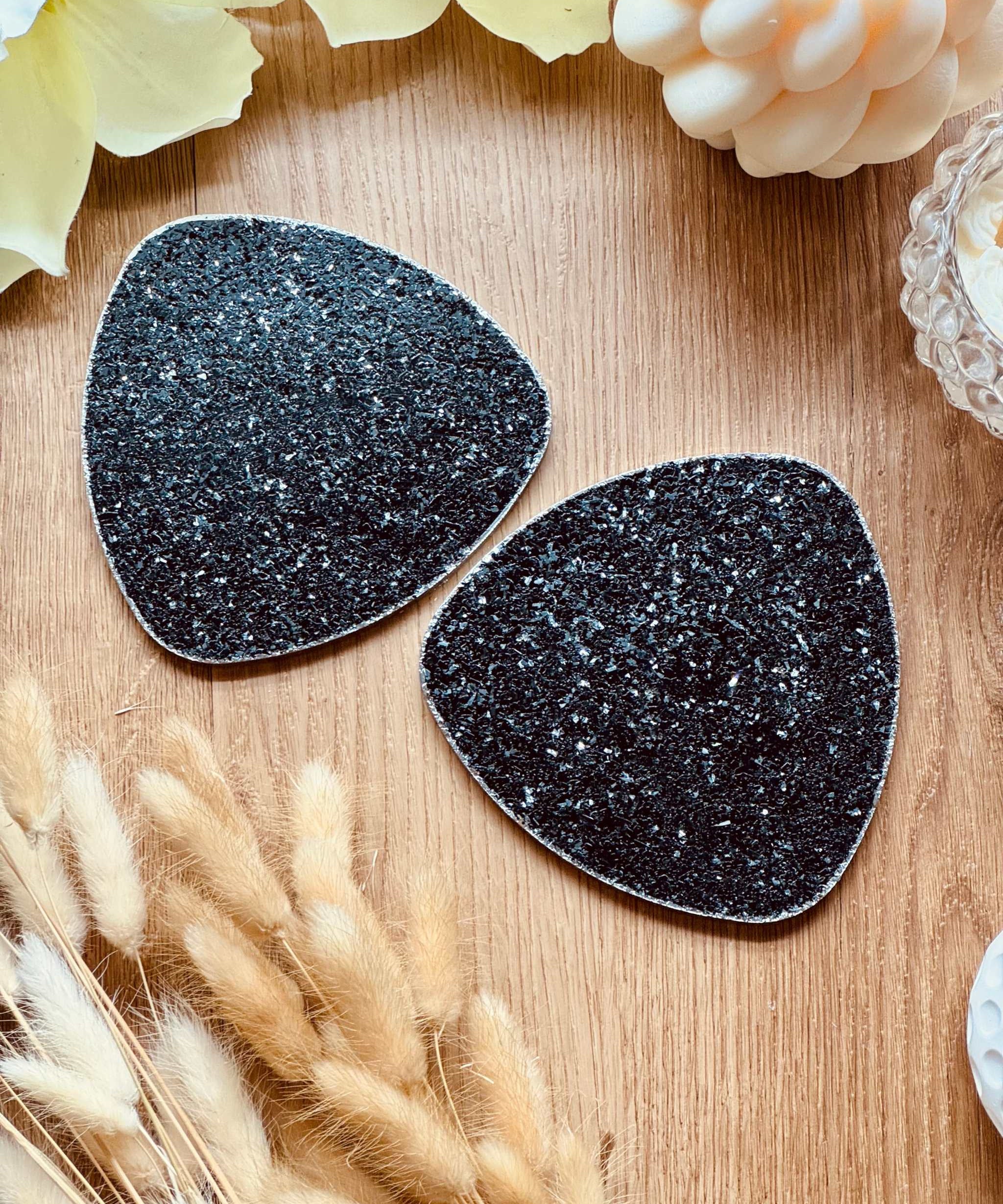 2 schwarze Untersetzer aus Resin mit silbernem Glitzer auf Holztisch dekorativ arrangiert
