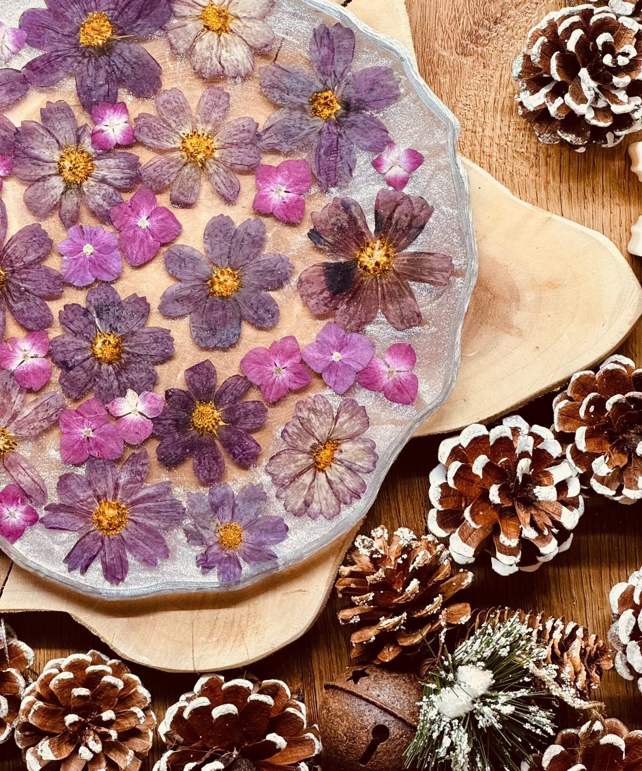 Handgemachtes Tablett aus Resin mit eingebetteten lila Hortensienblüten und silbernen Details, dekorativ auf Holzunterlage mit Kiefernzapfen arrangiert