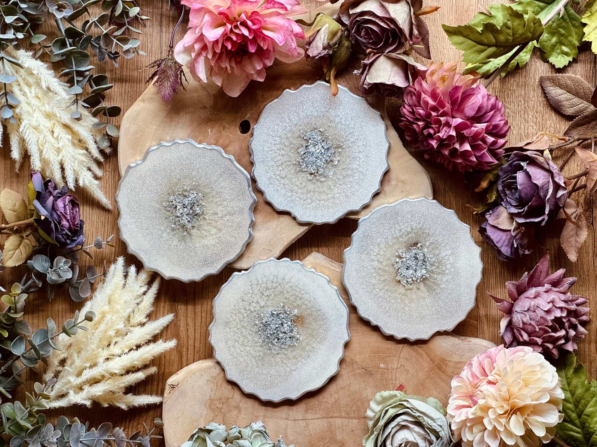 4 zeitlose Untersetzer aus weißem Resin mit silbernen Details auf Holztisch mit Dekoblumen