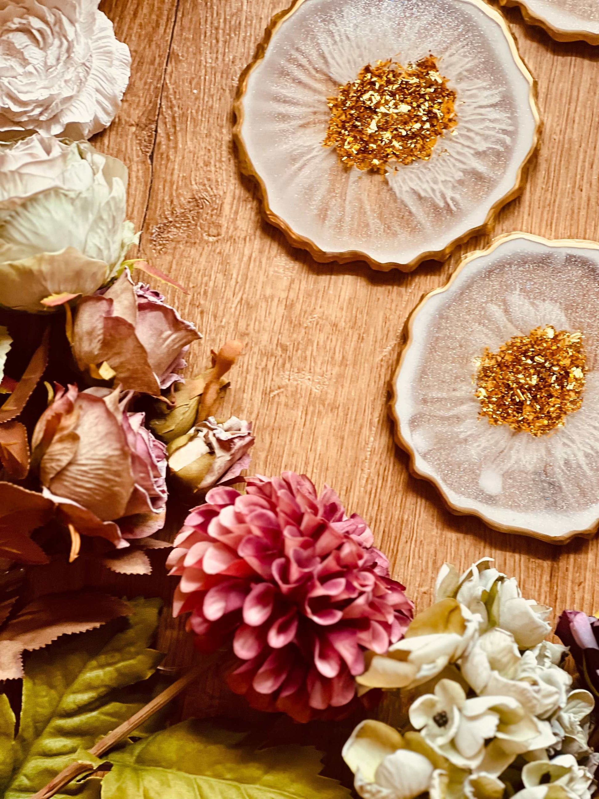 White resin coasters with gold accents, set of four, surrounded by flowers on a wooden table.