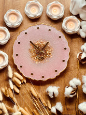 Handgefertigte Resin Uhr in Rosa mit goldenen Details und glitzerndem Zentrum auf Holzuntergrund mit dekorativen Kerzen und Trockenblumen