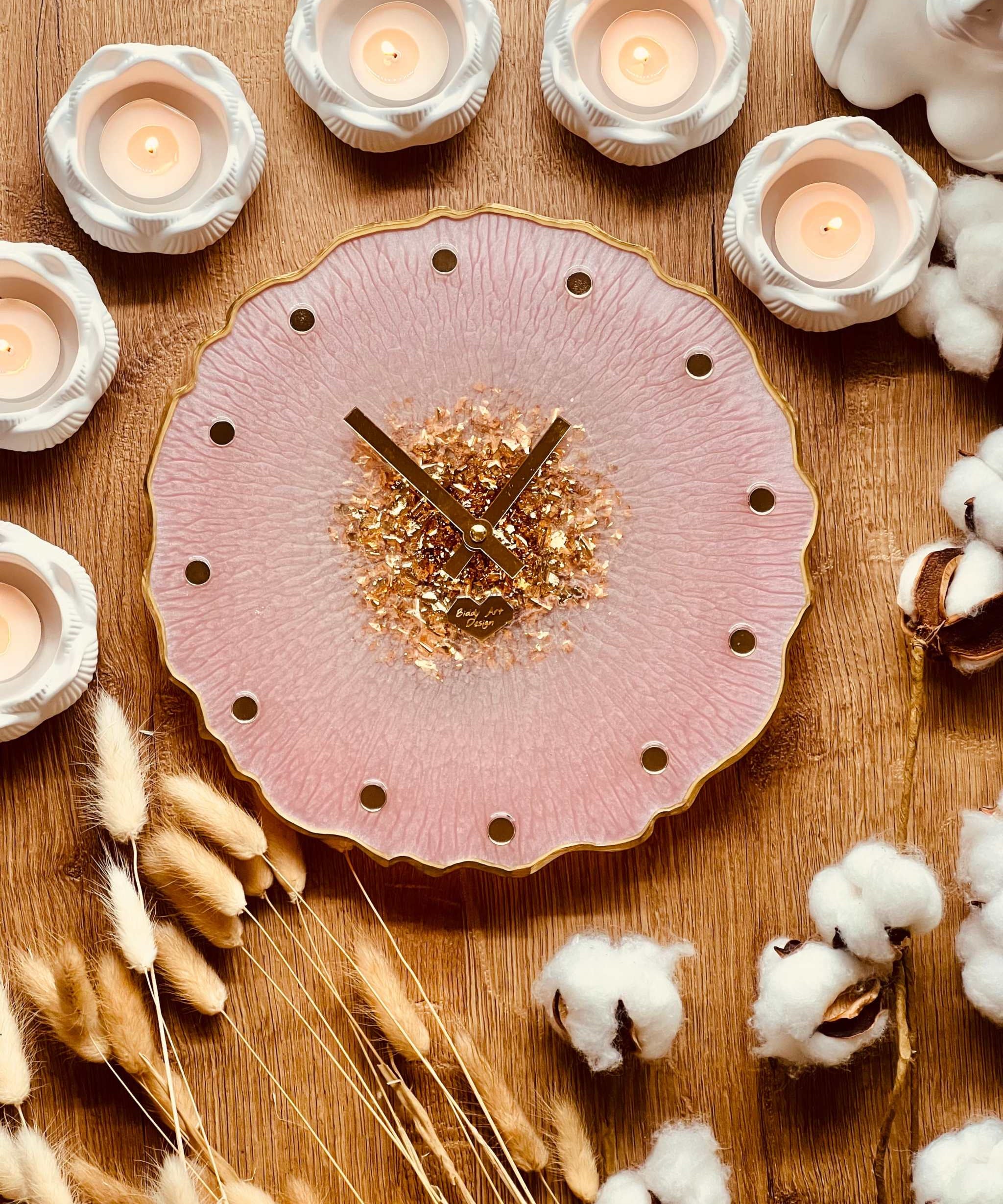 Handgefertigte Resin Uhr in Rosa mit goldenen Details und glitzerndem Zentrum auf Holzuntergrund mit dekorativen Kerzen und Trockenblumen