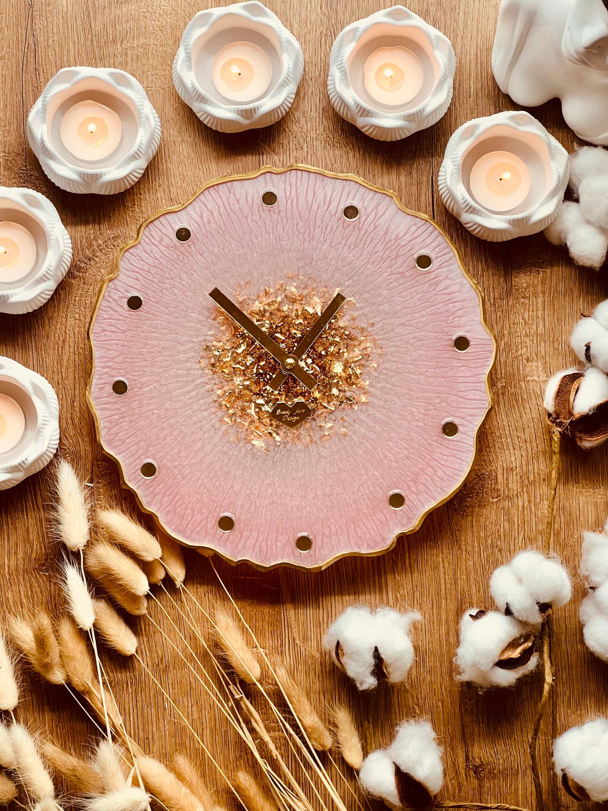 Handgefertigte Resin Uhr in Rosa mit goldenen Details und glitzerndem Zentrum auf Holzuntergrund mit dekorativen Kerzen und Trockenblumen