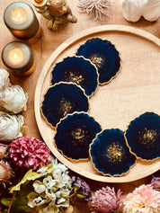 6 handgemachte blaue Resin Untersetzer mit goldenen Details auf rundem Holztablett und Blumenarrangement