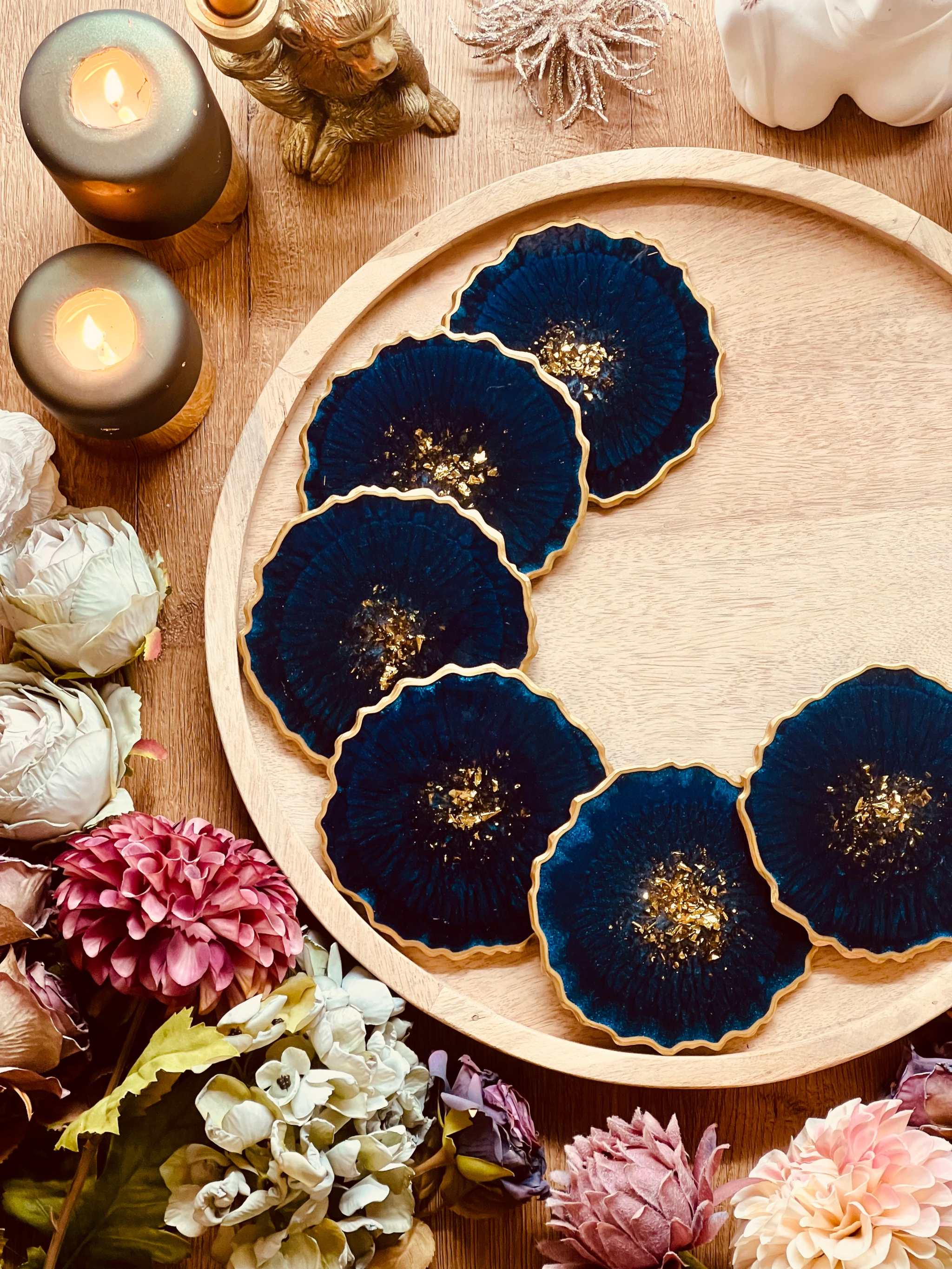 6 handgemachte blaue Resin Untersetzer mit goldenen Details auf rundem Holztablett und Blumenarrangement