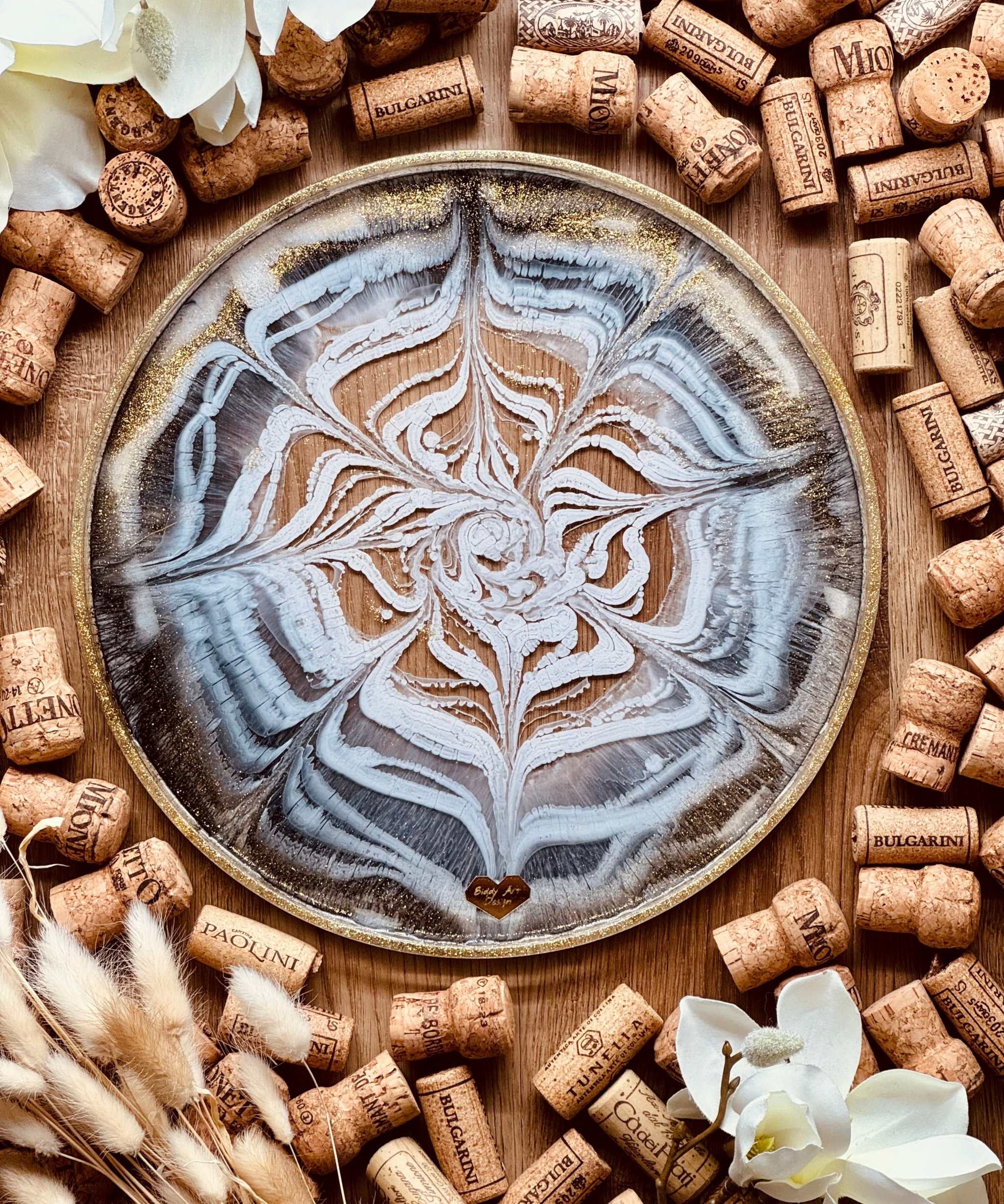 Handgemachtes schwarzes und weißes Resin Tablett mit goldenen Details und einzigartigem Muster, umgeben von Korken und weißen Blüten.