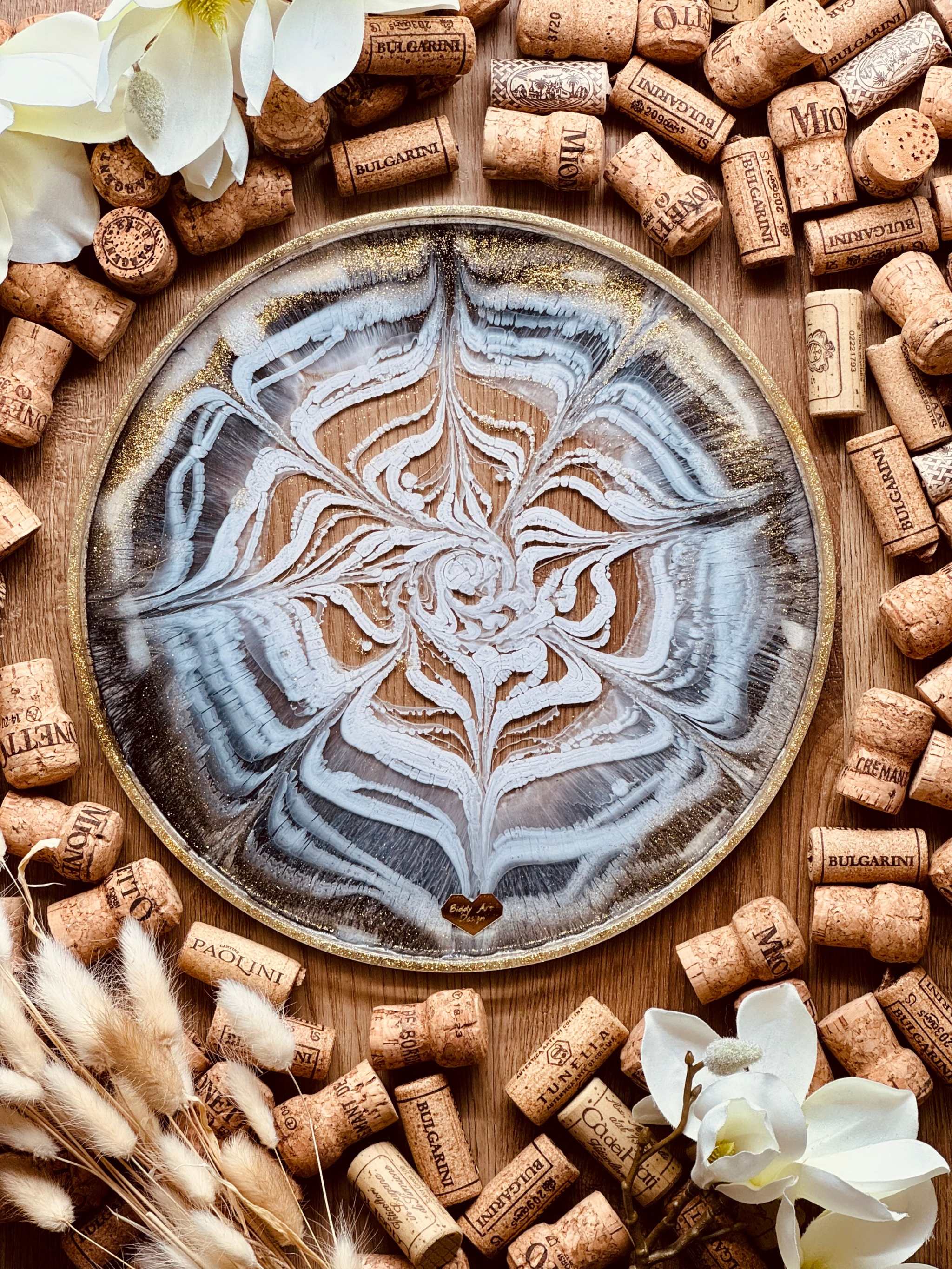 Handgemachtes schwarzes und weißes Resin Tablett mit goldenen Details und einzigartigem Muster, umgeben von Korken und weißen Blüten.