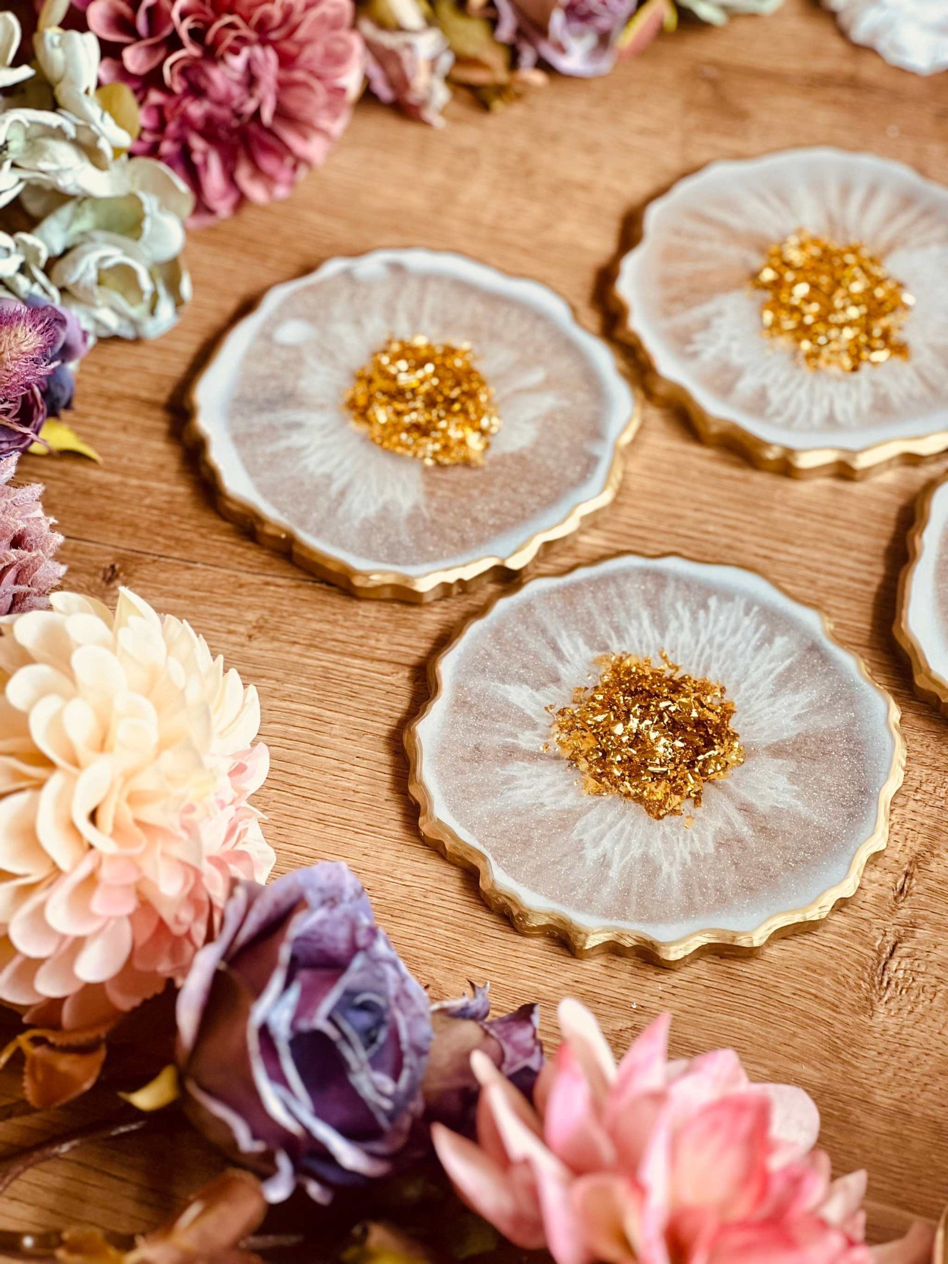 Vier glamouröse weiße Resin-Untersetzer mit goldenen Details.