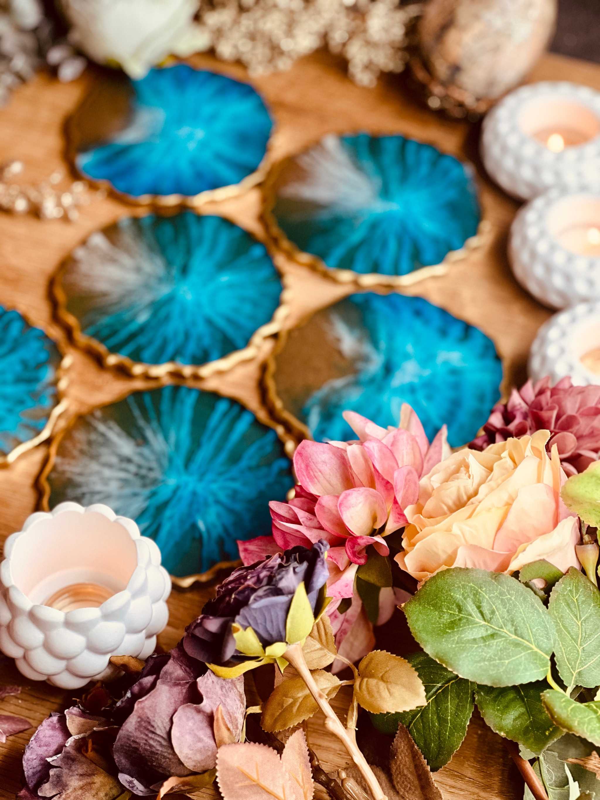 Set aus 6 handgemachten blauen Untersetzern aus Resin mit goldenen Akzenten im Ocean Design auf Holztisch mit Blumen und Kerzen