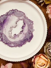 Tablett aus Resin im handgemachten Geode Kristall Design mit violetten Farbverläufen auf rundem weißem Untergrund umgeben von Rosenblüten