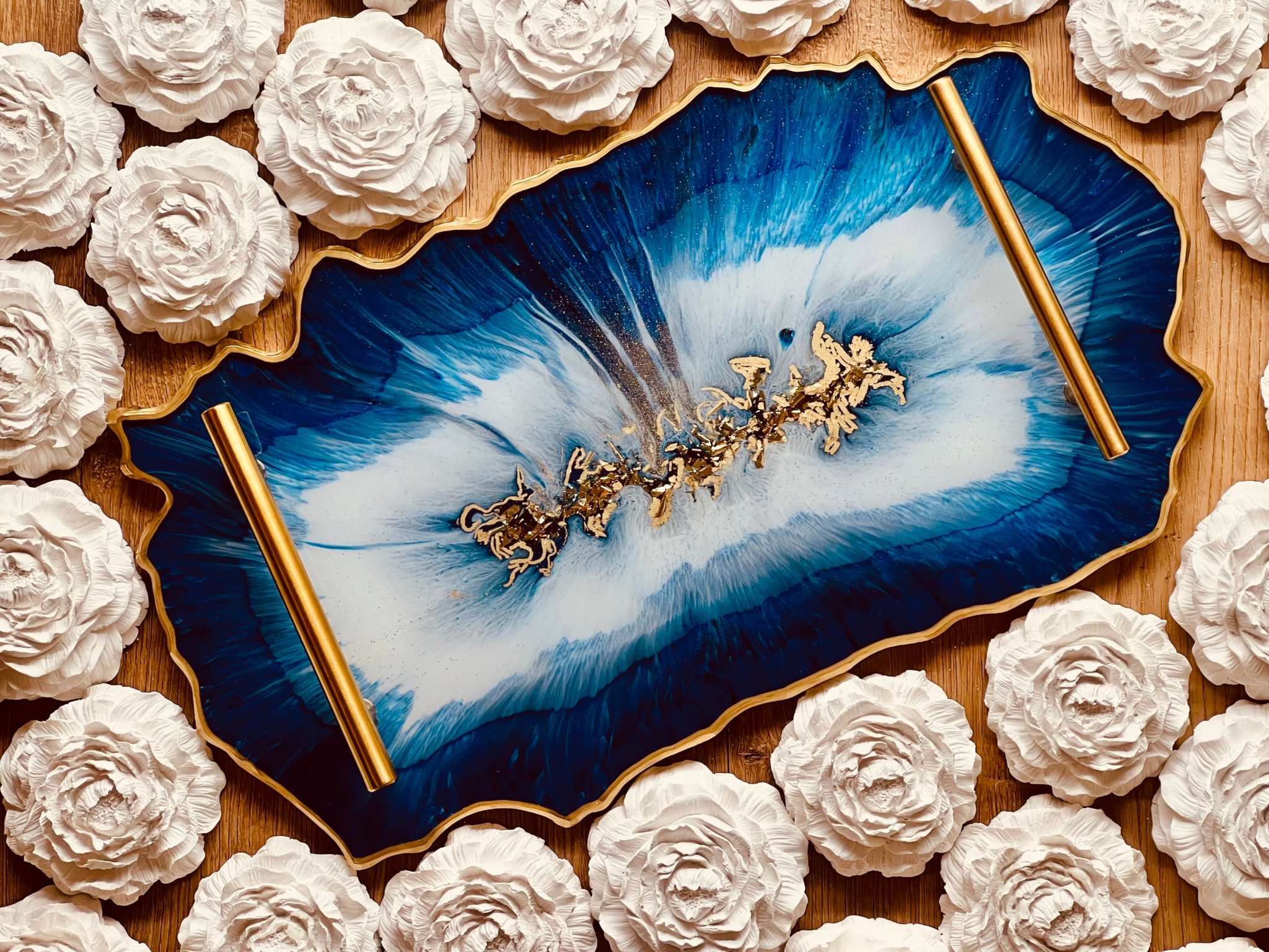 Handgemachtes blau-weißes Resin-Tablett mit goldenen Details und dekorativen Griffen, umgeben von weißen Rosen aus Gips.