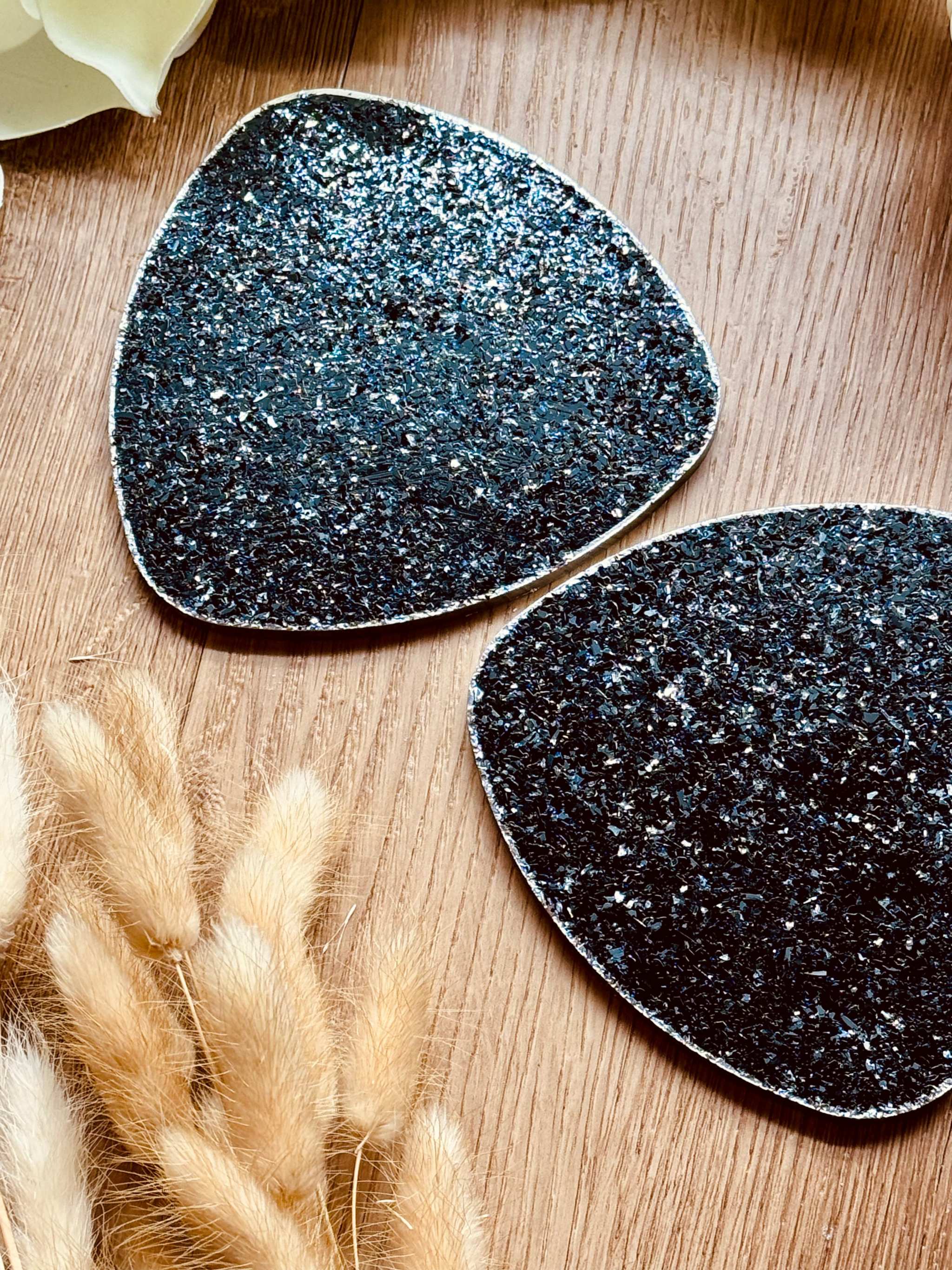 Zwei handgemachte schwarze Untersetzer aus Resin mit silberner Glitzeroberfläche auf Holztisch