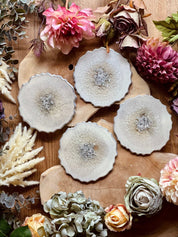 4 zeitlose Untersetzer aus weißem Resin mit silbernen Details auf Holztisch mit Blumen dekoriert