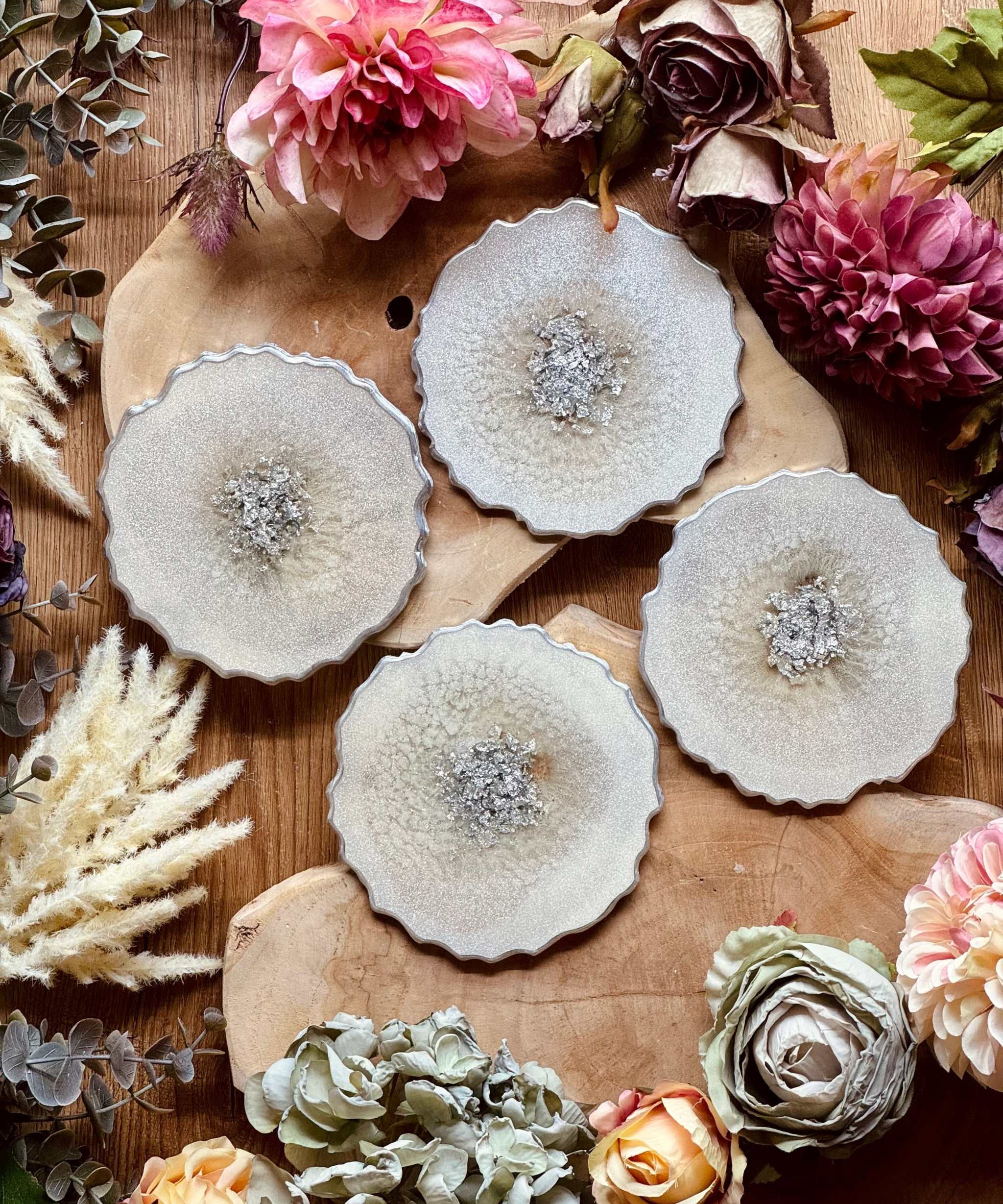 4 zeitlose Untersetzer aus weißem Resin mit silbernen Details auf Holztisch mit Blumen dekoriert