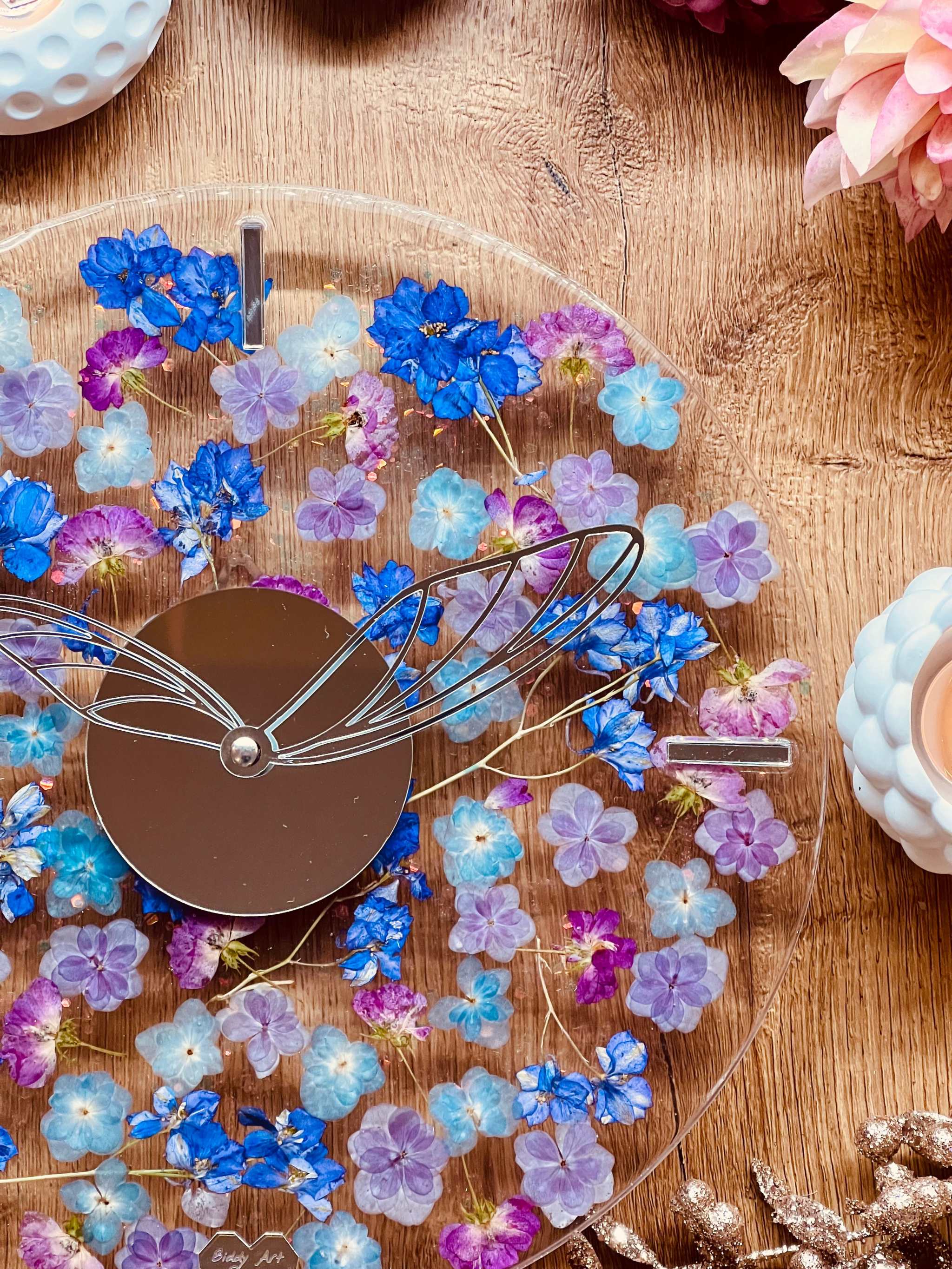 Handgefertigte Resin Uhr mit getrockneten blauen und lila Blumen und Glitzer auf Holzoberfläche