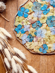 Handgemachtes Tablett aus Resin mit blauen und gelben Hortensien und silbernen Details auf Holzuntergrund