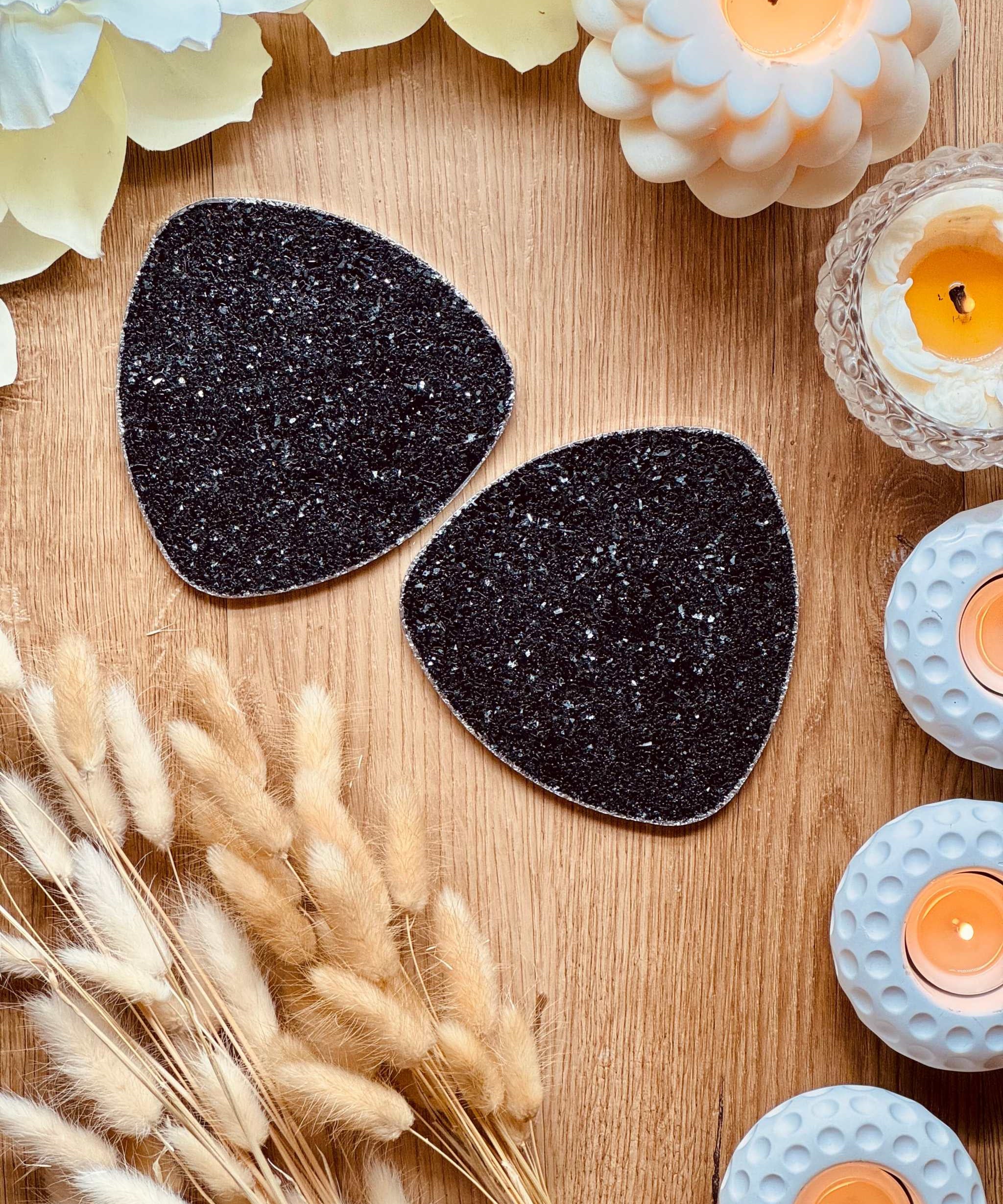 Zwei handgemachte Untersetzer aus Resin in Schwarz mit silbernem Glitzer auf Holztisch und Kerzen dekoriert
