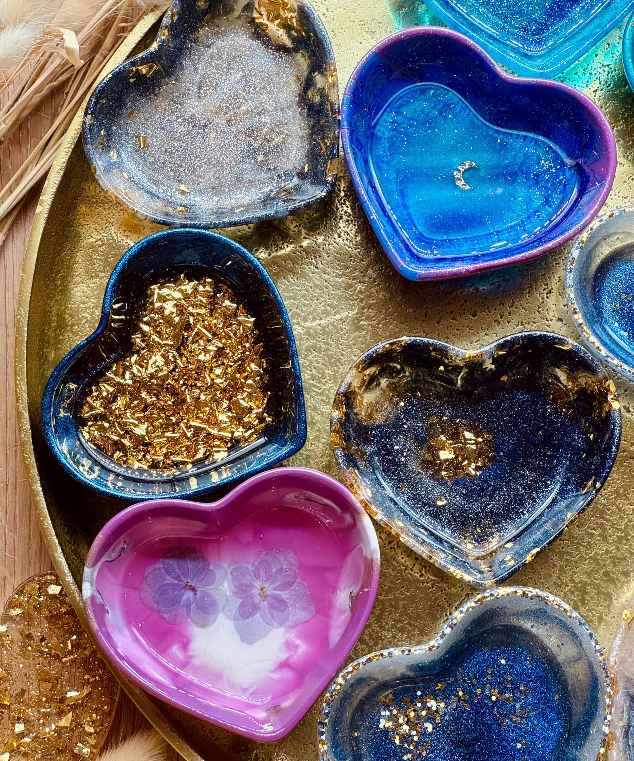 bunte handgemachte herzförmige Schmuckschalen aus Resin mit goldenen Details auf goldfarbenem Tablett
