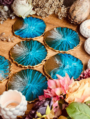 6 handgemachte Untersetzer aus Resin in Blau mit goldenen Akzenten im Ocean Design auf Holztisch mit Blumen arrangiert