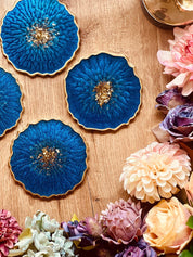 4 Untersetzer aus Resin in Blau mit goldenen Details auf Holz mit Blumenarrangement