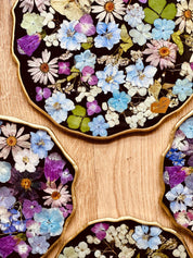 handgemachtes Tablett aus Resin mit getrockneten Blumen und goldenen Details auf Holzoberfläche