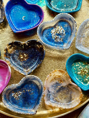 Bunte handgemachte Schmuckschalen aus Resin mit goldenen Details in Herzform auf goldenem Tablett
