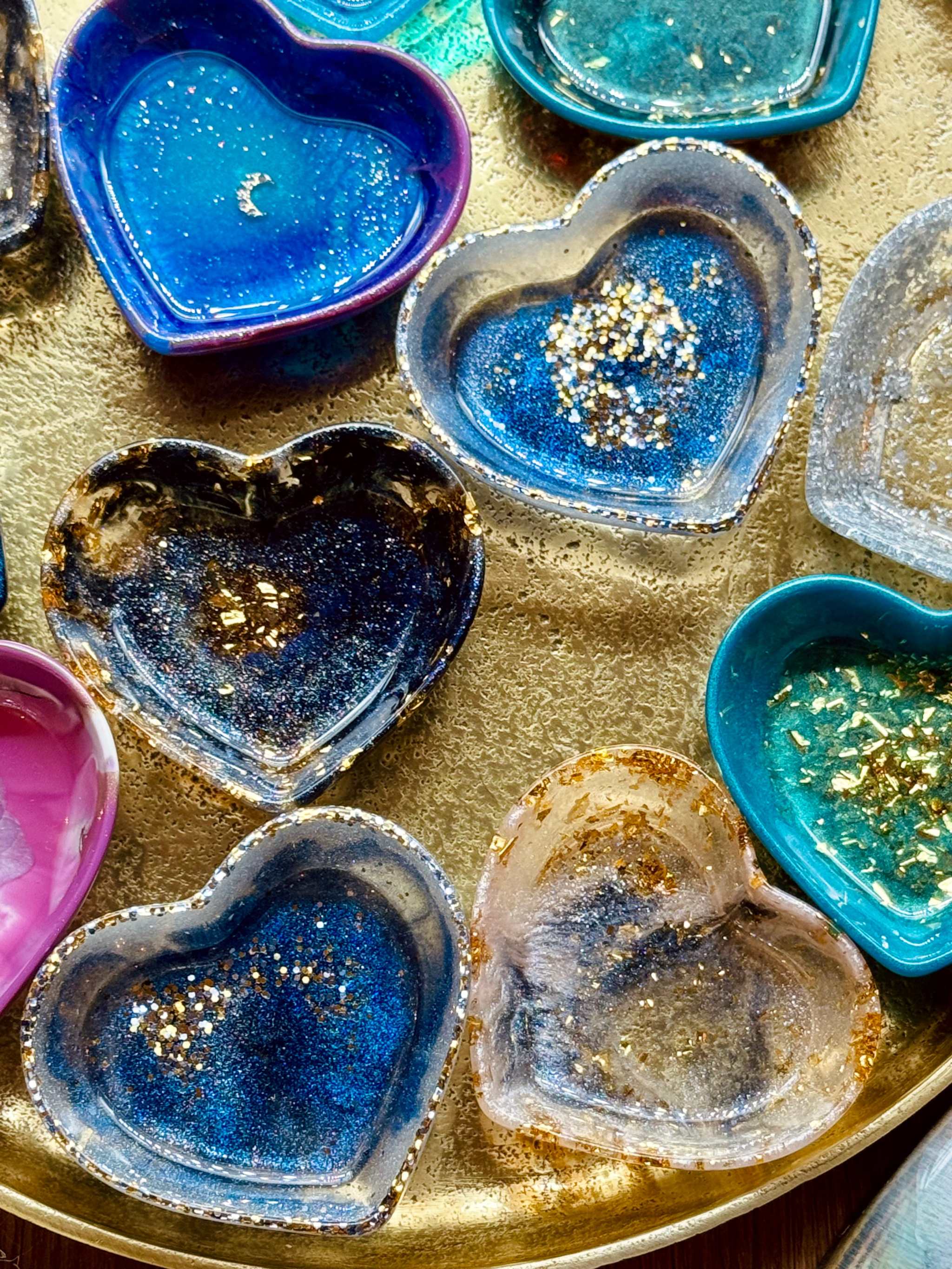 Bunte handgemachte Schmuckschalen aus Resin mit goldenen Details in Herzform auf goldenem Tablett