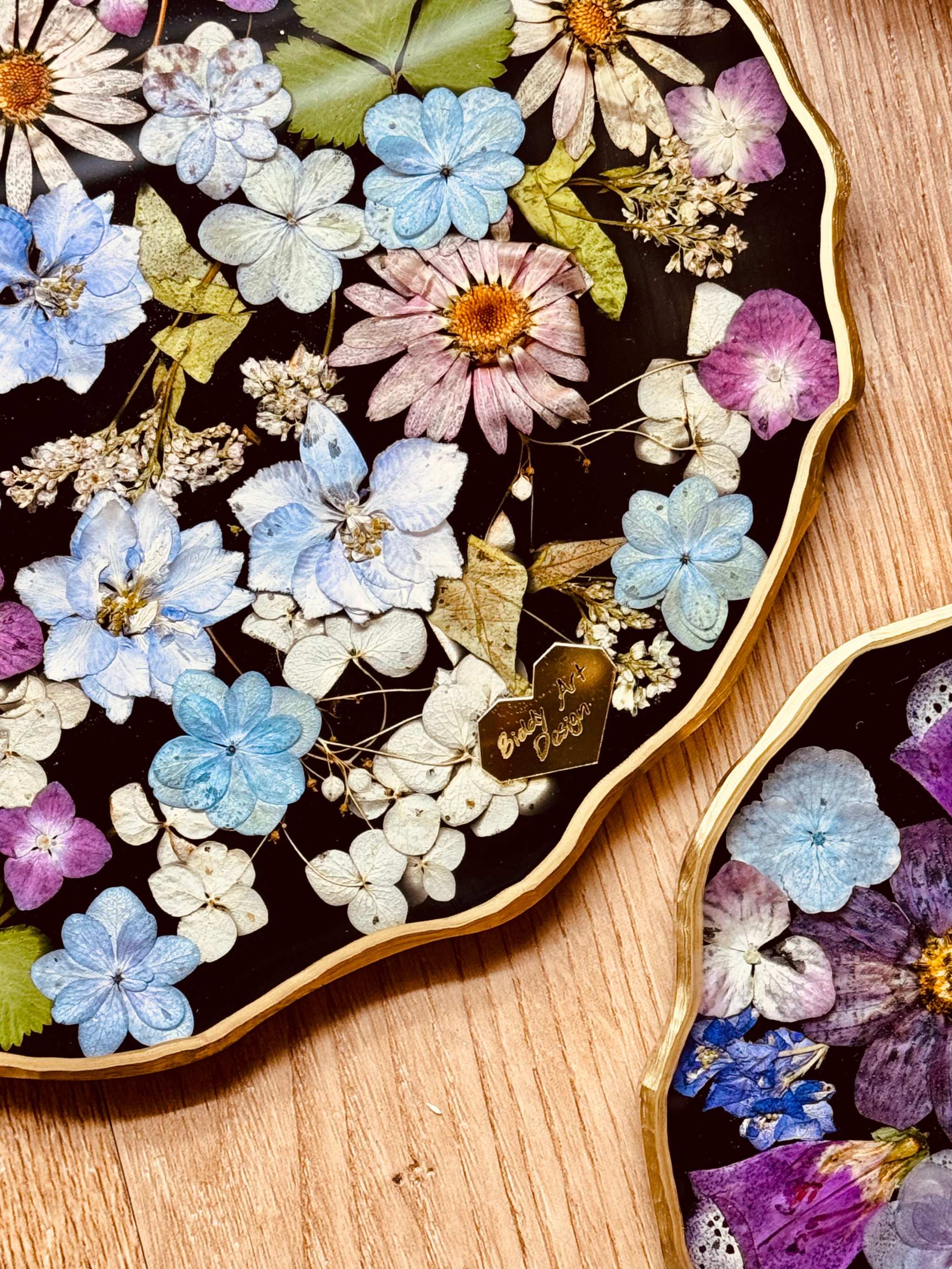 Handgemachtes Tablett aus Resin mit getrockneten Blumen und goldenen Details auf Holzuntergrund
