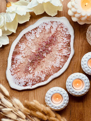 Handgemachtes rosa Tablett aus Resin mit silbernen Details auf Holzoberfläche neben Kerzen und weißen Deko-Blüten