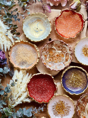 bunte handgemachte Schmuckschalen aus Resin mit goldenen Details und unregelmäßigen Rändern auf Holztisch mit Dekopflanzen