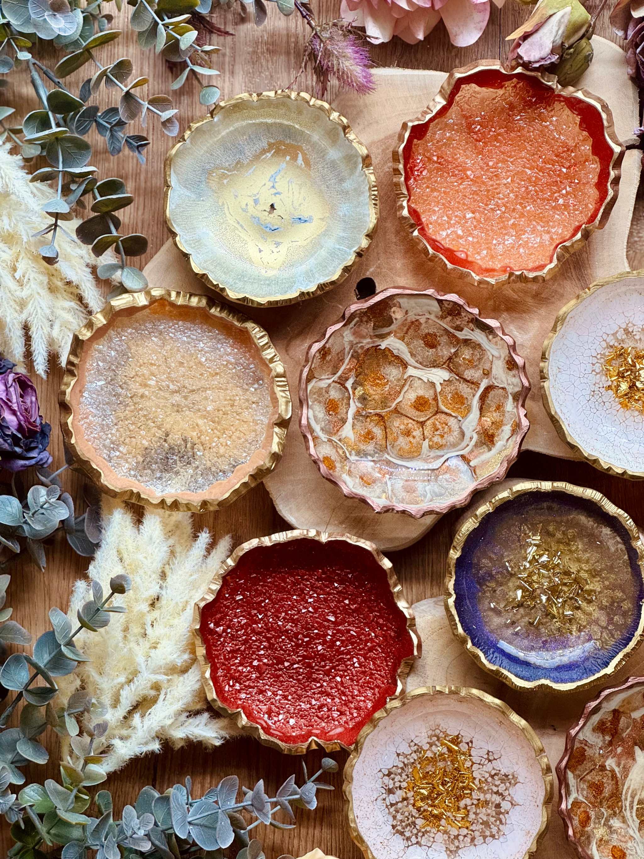 bunte handgemachte Schmuckschalen aus Resin mit goldenen Details und unregelmäßigen Rändern auf Holztisch mit Dekopflanzen