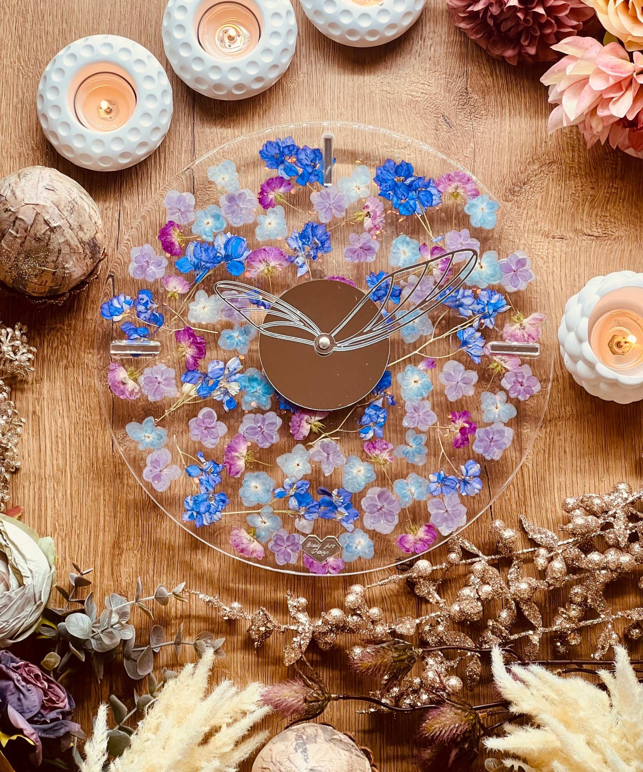 Handgemachte Resin Uhr mit getrockneten blauen und lila Blumen und Glitzer auf Holztisch mit Kerzen und Dekoration