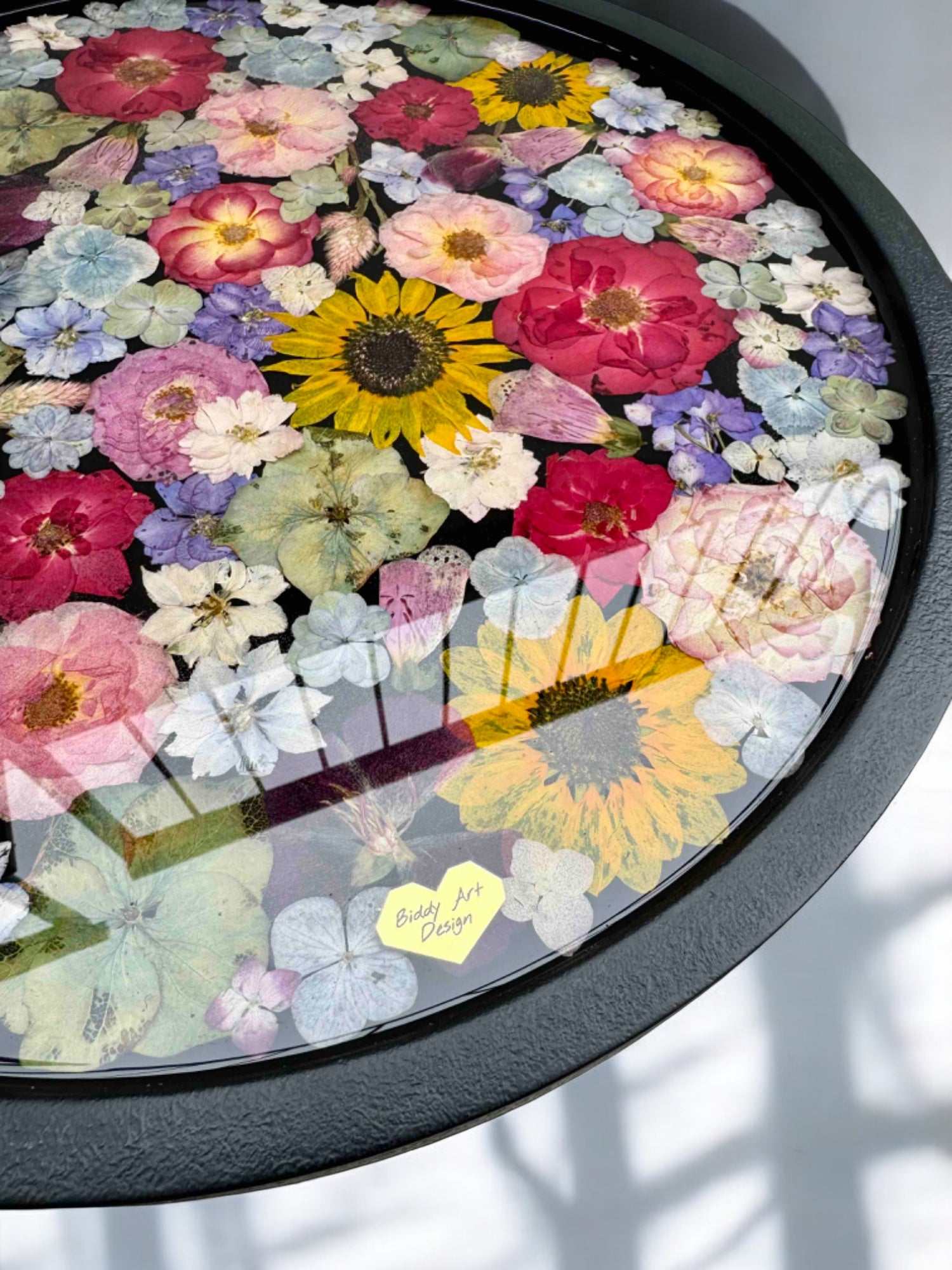 Brautstrauß konservieren -  Detailaufnahme eines Couchtischs mit schwarzer Holzplatte, goldfarbenem Gestell und in Epoxidharz gegossenen echten Blumen – farbenfroh und einzigartig.Auch mit deinem Brautstrauß zur Brautstrauss Konservierung