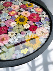 Brautstrauß konservieren -  Detailaufnahme eines Couchtischs mit schwarzer Holzplatte, goldfarbenem Gestell und in Epoxidharz gegossenen echten Blumen – farbenfroh und einzigartig.Auch mit deinem Brautstrauß zur Brautstrauss Konservierung