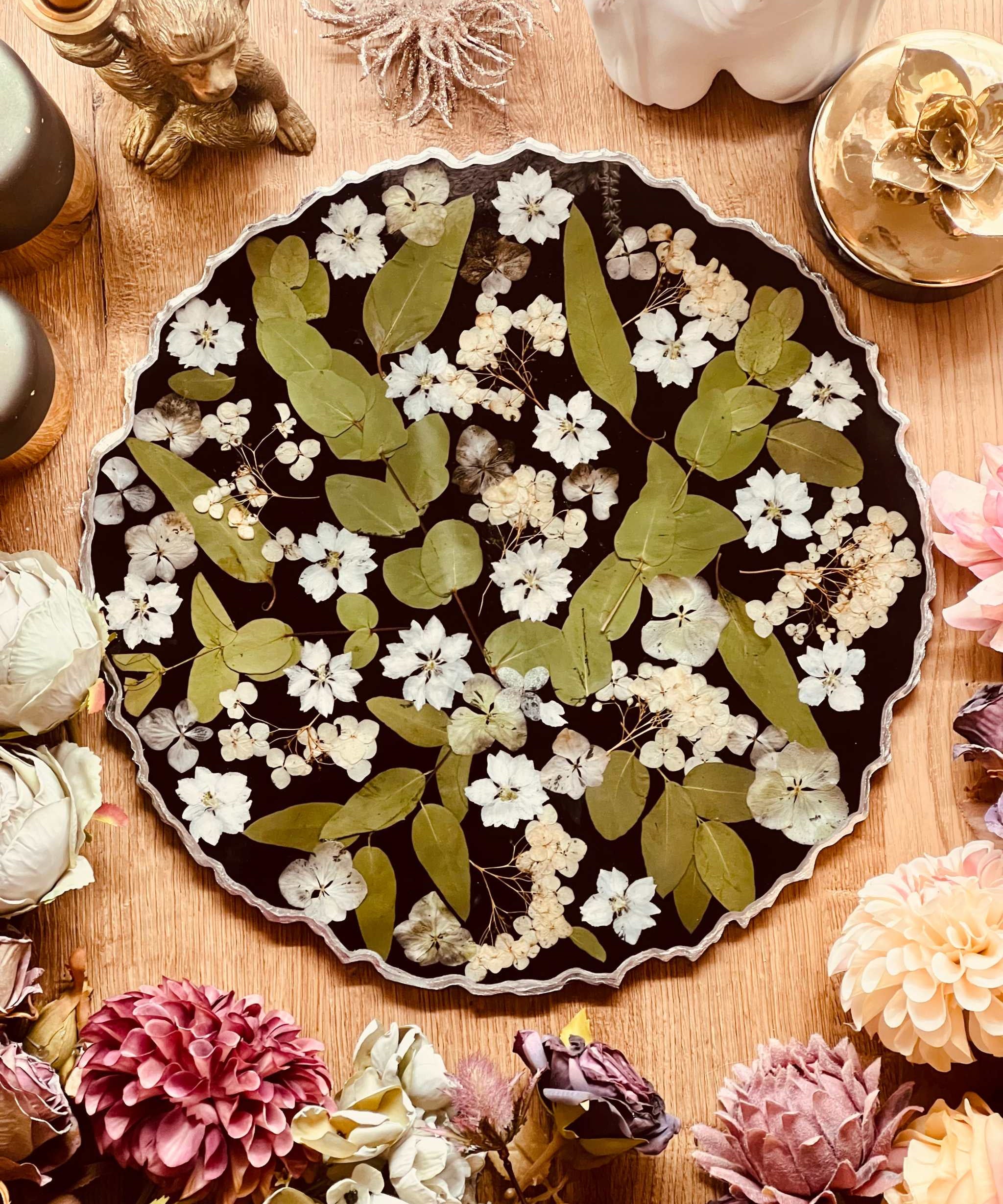 Rundes handgemachtes Tablett aus schwarzem Resin mit eingelegten Hortensien, Eukalyptusblättern und silbernen Details, dekorativ auf Holztisch