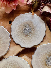 4 zeitlose Untersetzer aus weißem Resin mit silbernen Details auf Holztisch mit Blütenarrangement
