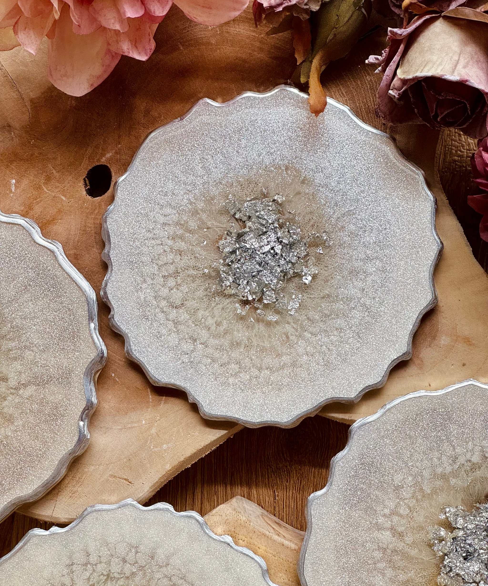 4 zeitlose Untersetzer aus weißem Resin mit silbernen Details auf Holztisch mit Blütenarrangement